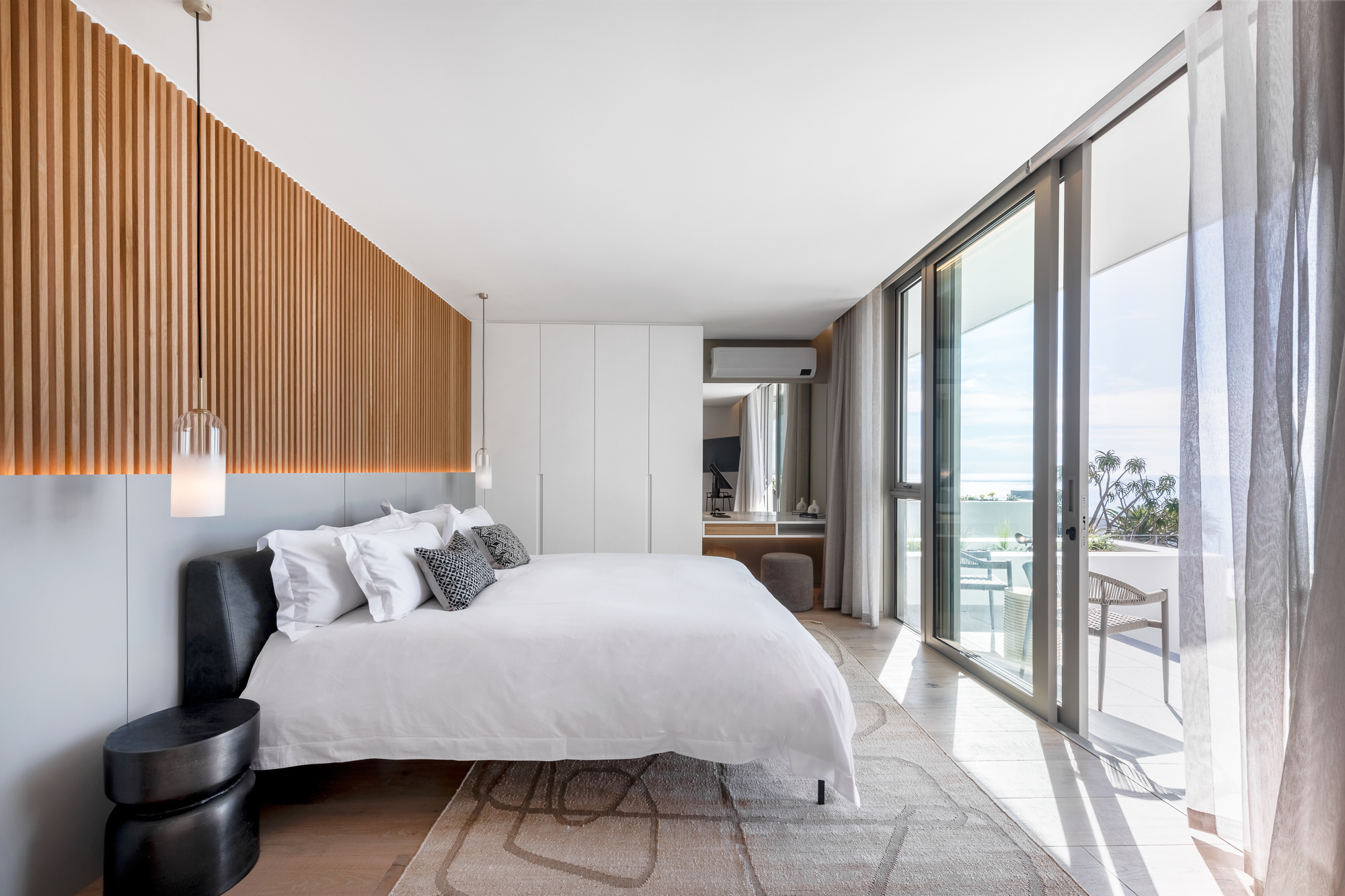 Luna Suite bedroom with wood-slat headboard and sea-view balcony – Riva One, Camps Bay