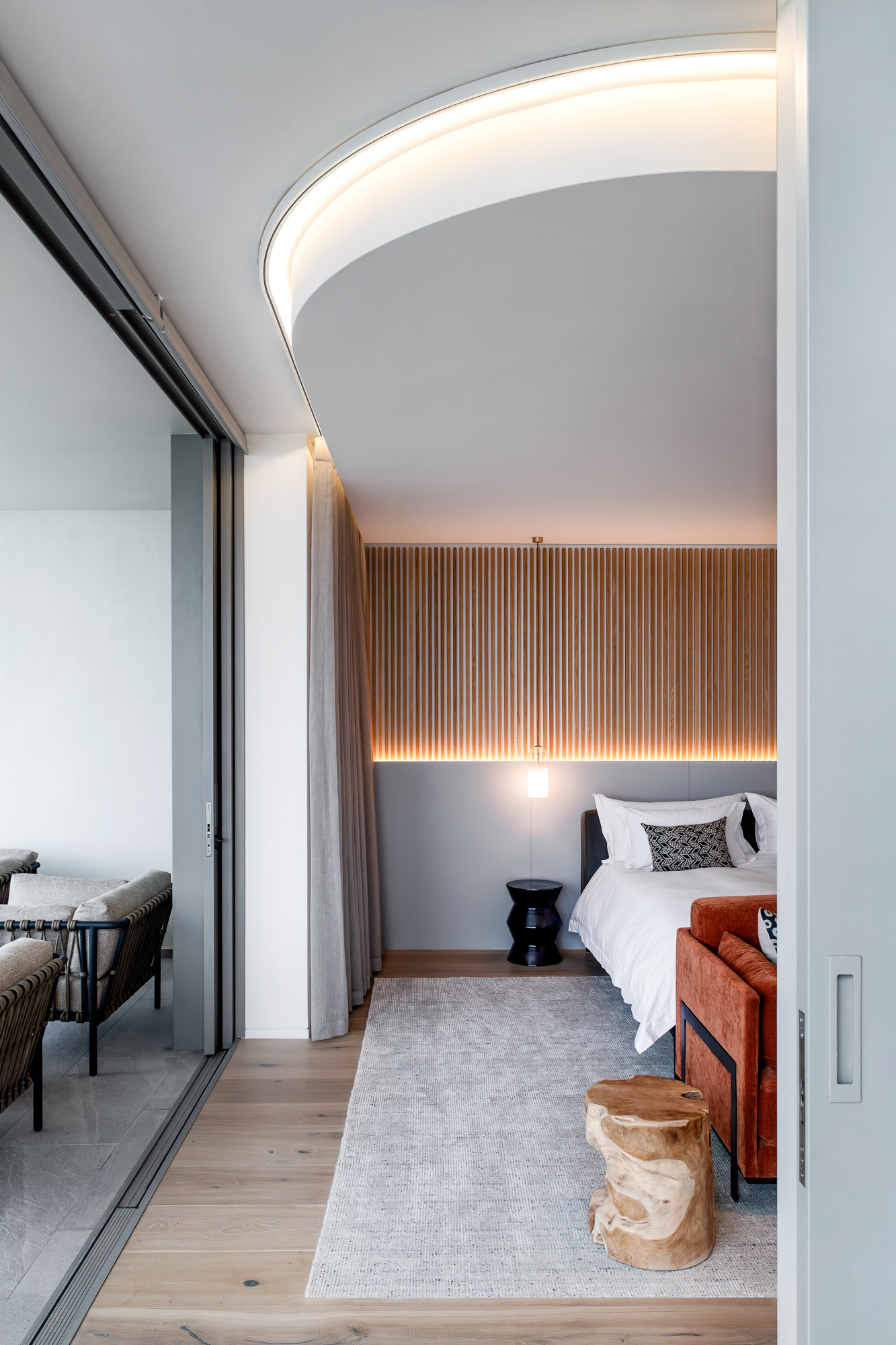 Sole Suite bedroom with curved cove-lit ceiling, wood-slat headboard and balcony views – Riva One, Camps Bay