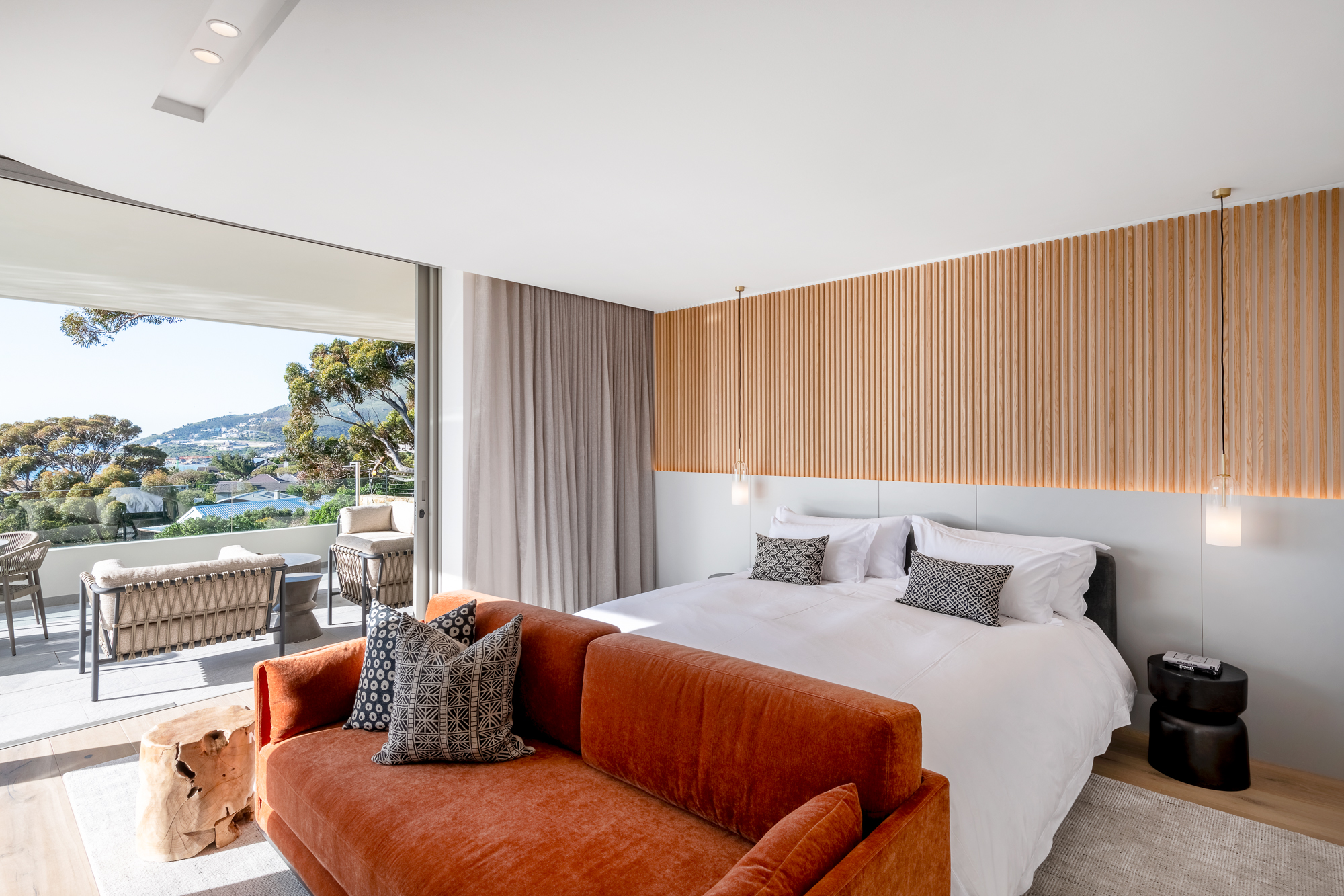 Sole Suite bedroom with wood-slat headboard wall and glass doors to the sea-view balcony – Riva One, Camps Bay